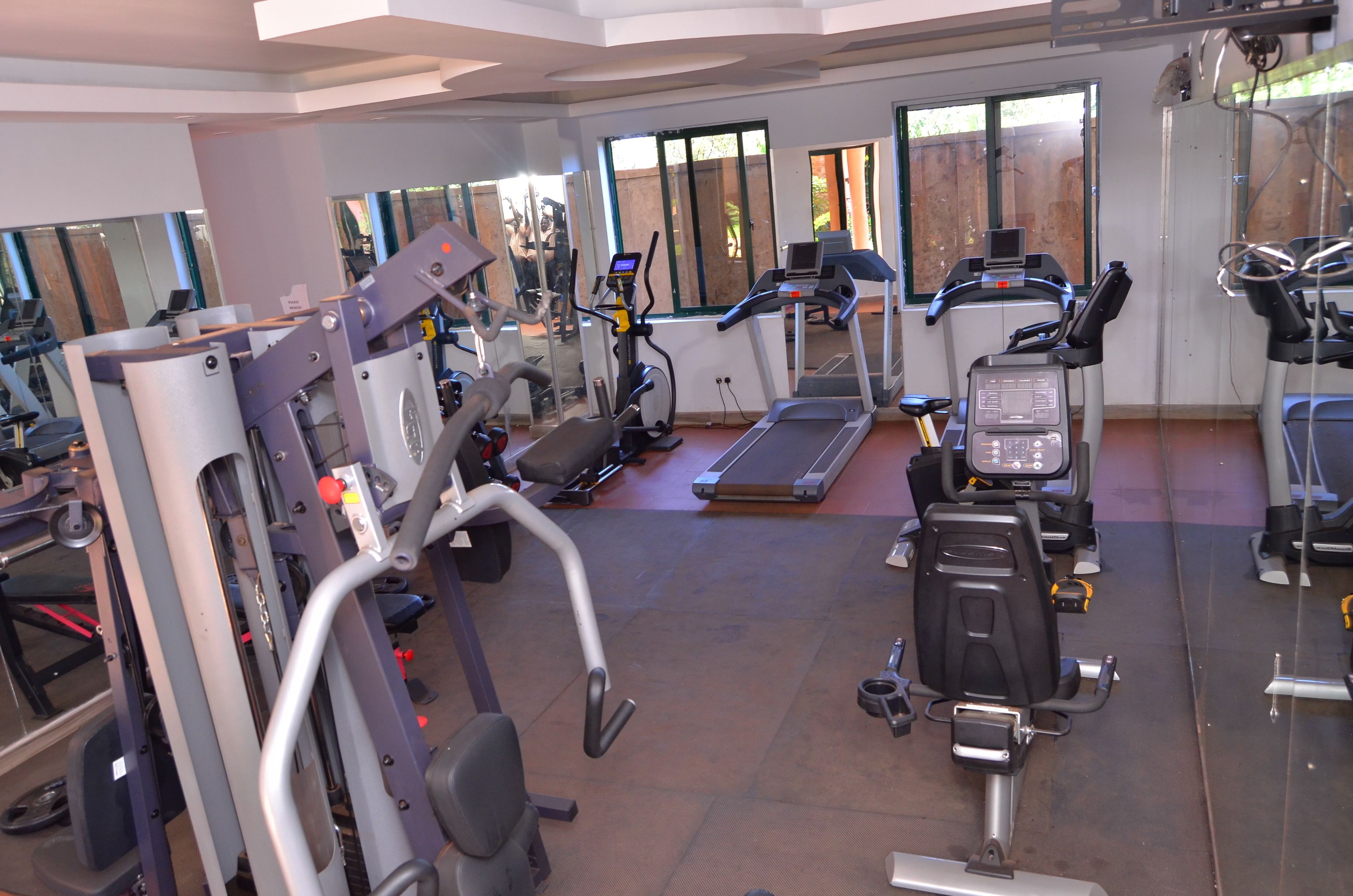 Un gimnasio con diversas máquinas de ejercicio, una cinta de correr y un muro con espejos.