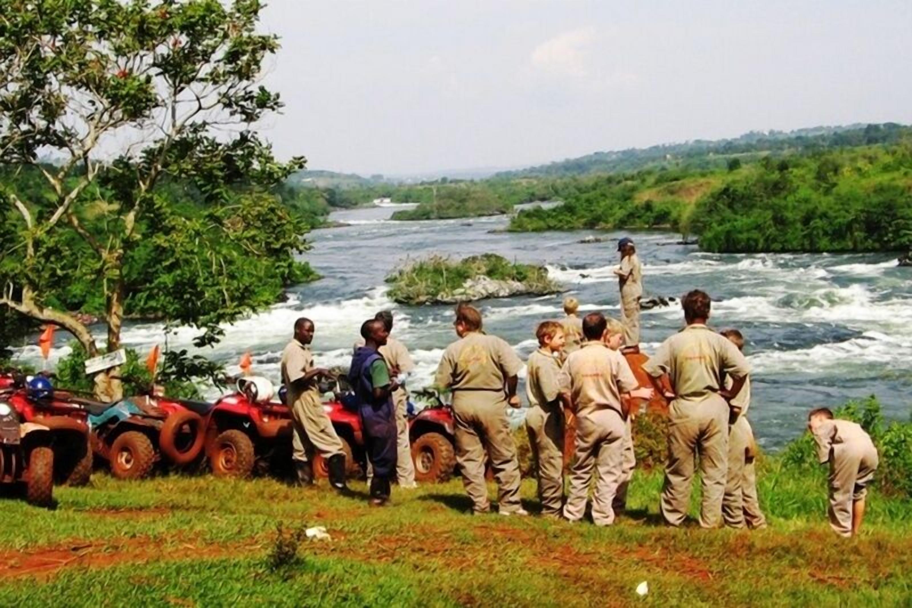 Un grupo de personas cerca de un río, algunas sobre vehículos todo terreno, con un paisaje verde exuberante al fondo.