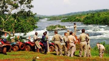 Un grupo de personas cerca de un río, algunas sobre vehículos todo terreno, con un paisaje verde exuberante al fondo.