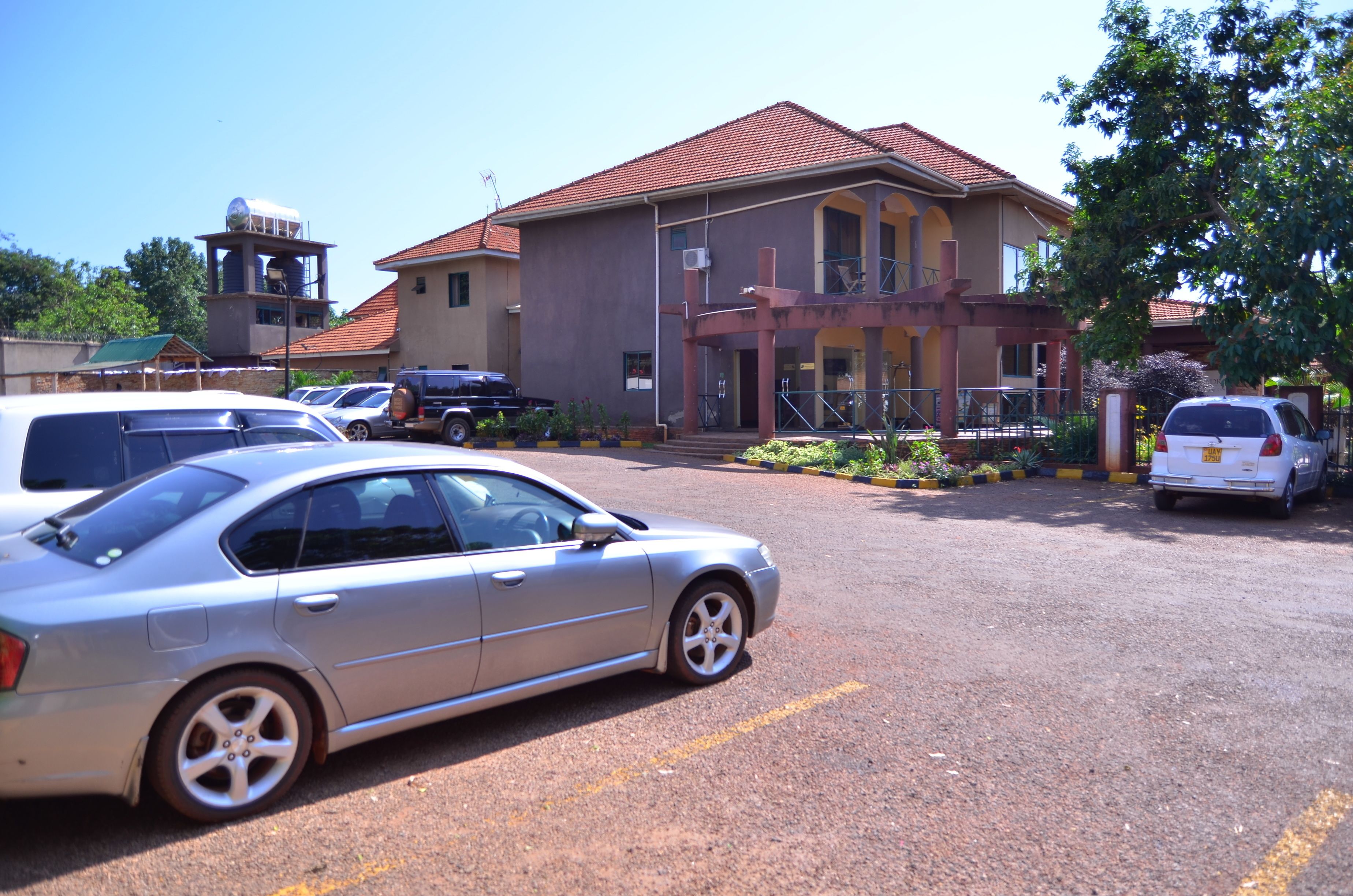A parking lot with several cars, a building with a red roof, and a water tower in the background.