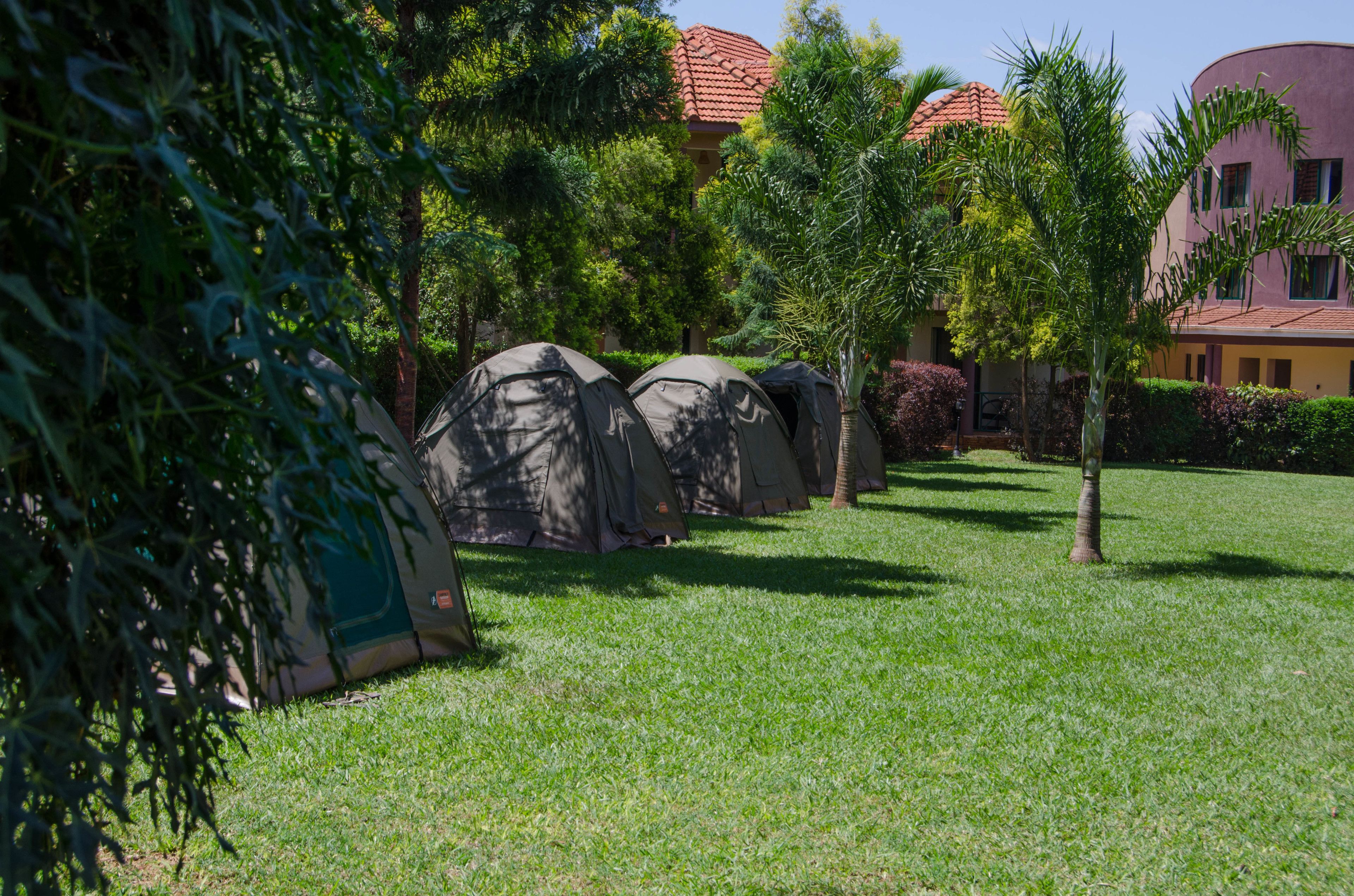 A grassy area with several tents and a building with a red-tiled roof in the background.