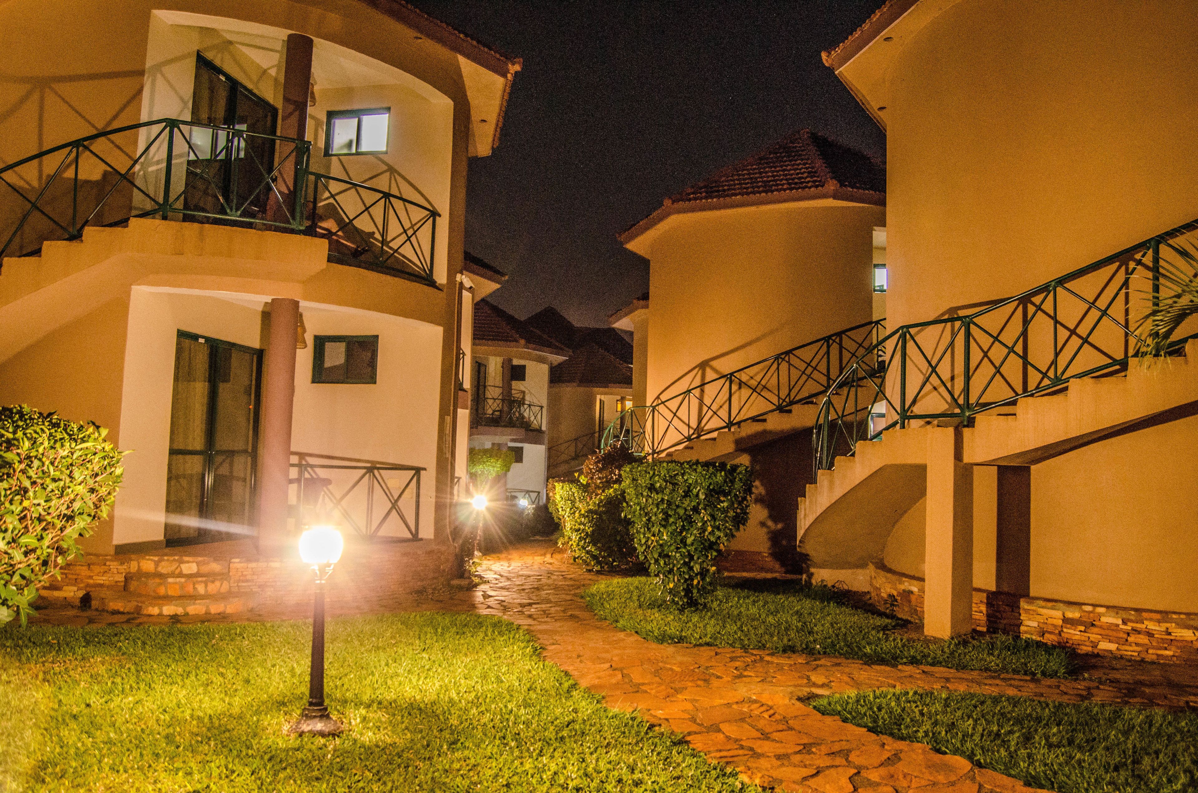 Une vue nocturne d’un immeuble d’habitation doté de nombreux balcons, d’un chemin en pierre et d’un lampadaire illuminé.
