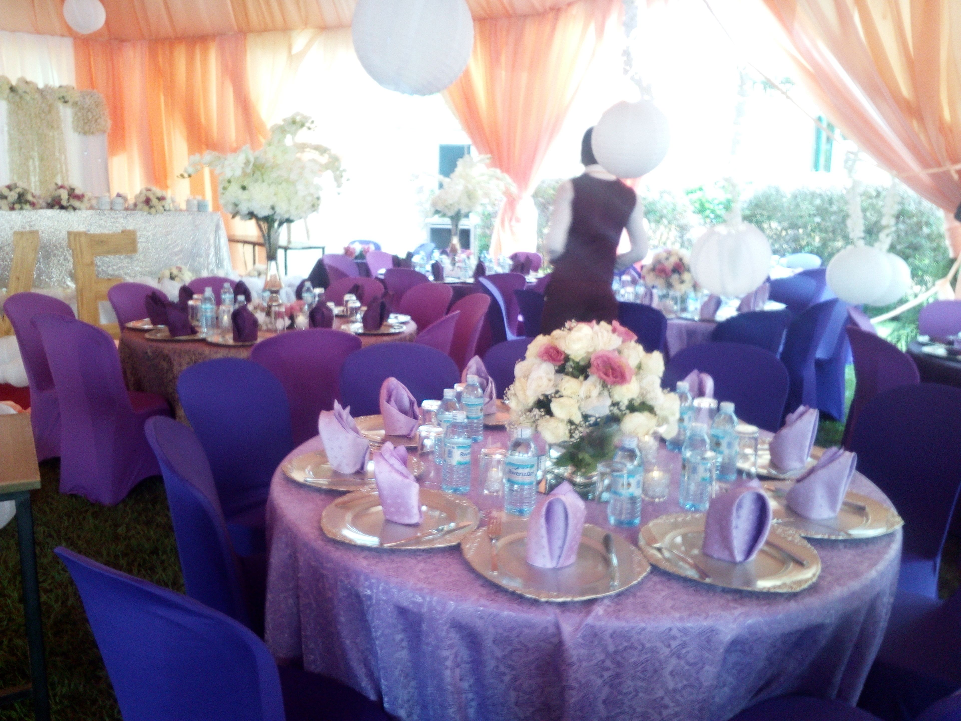 A banquet hall with round tables covered in purple tablecloths, surrounded by purple chairs.