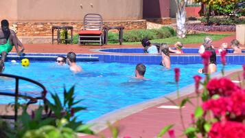 Un espace piscine où des personnes nagent et s’amusent, entouré d’un mur de pierre et de quelques plantes.