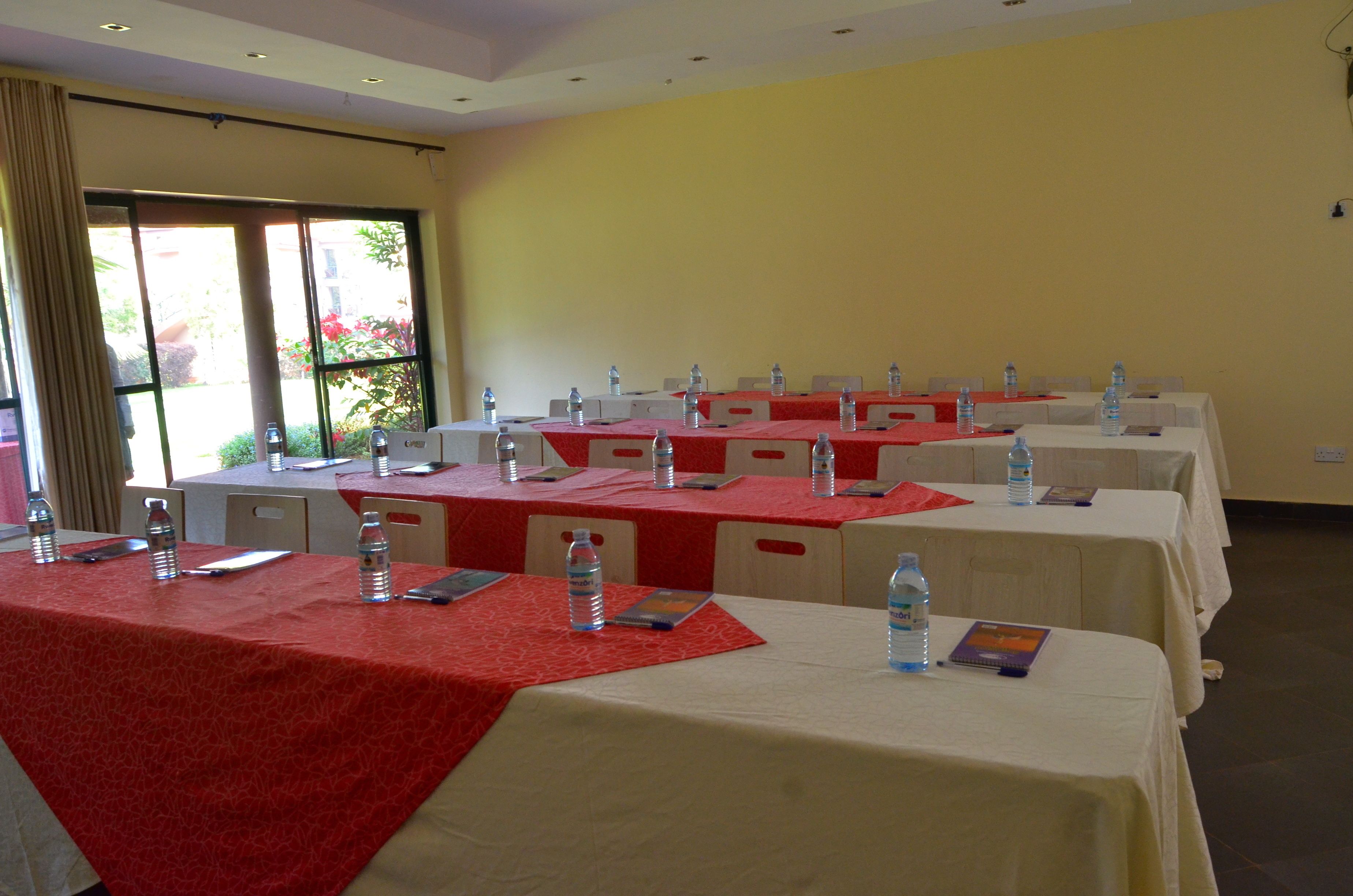 Une salle de conférence dotée de plusieurs tables, chacune recouverte d’une nappe rouge et équipée de bouteilles d’eau et de porte-noms.