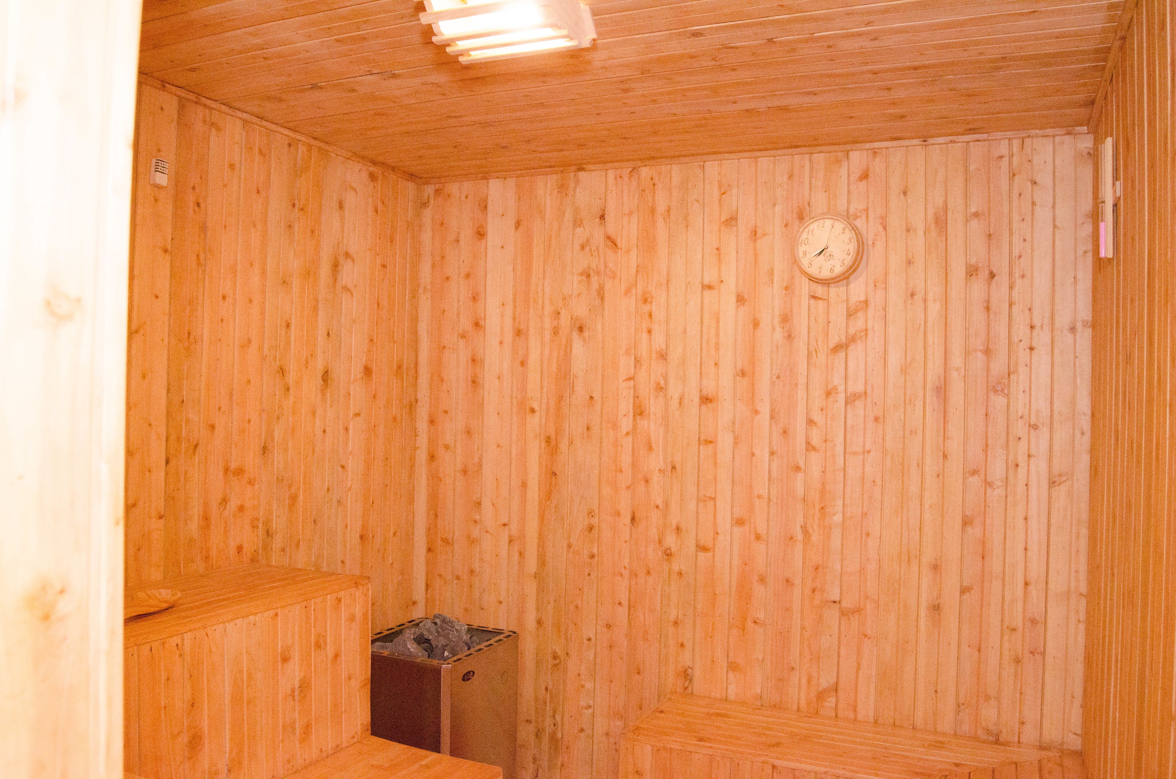 A wooden sauna with a wooden bench, a small heater, and a wall-mounted clock.