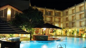 Zona de piscina hotelera con jacuzzi, sillas de descanso y un área de estar techada.