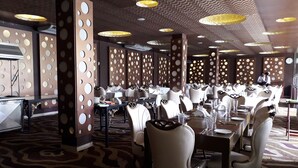 Un restaurante con mesas redondas, sillas blancas y una alfombra estampada.