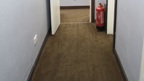 A narrow hallway with a patterned carpet, a fire extinguisher, and a door at the end. - The Angus Hotel (London)