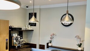 A modern reception area with a wooden counter, a coffee machine, and a clock on the wall. - The Angus Hotel (London)