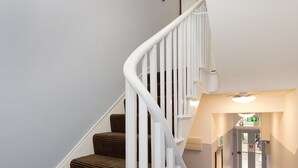 A staircase with a white railing leading to a landing. - The Angus Hotel (London)