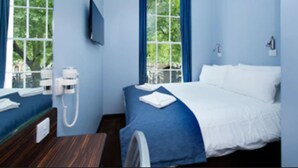 A hotel room with a bed, a bedside table, a TV mounted on the wall, and a window with curtains. - The Angus Hotel (London)