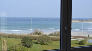Blick auf das Meer durch ein Fenster, im Vordergrund eine Rasenfläche und eine Straße.