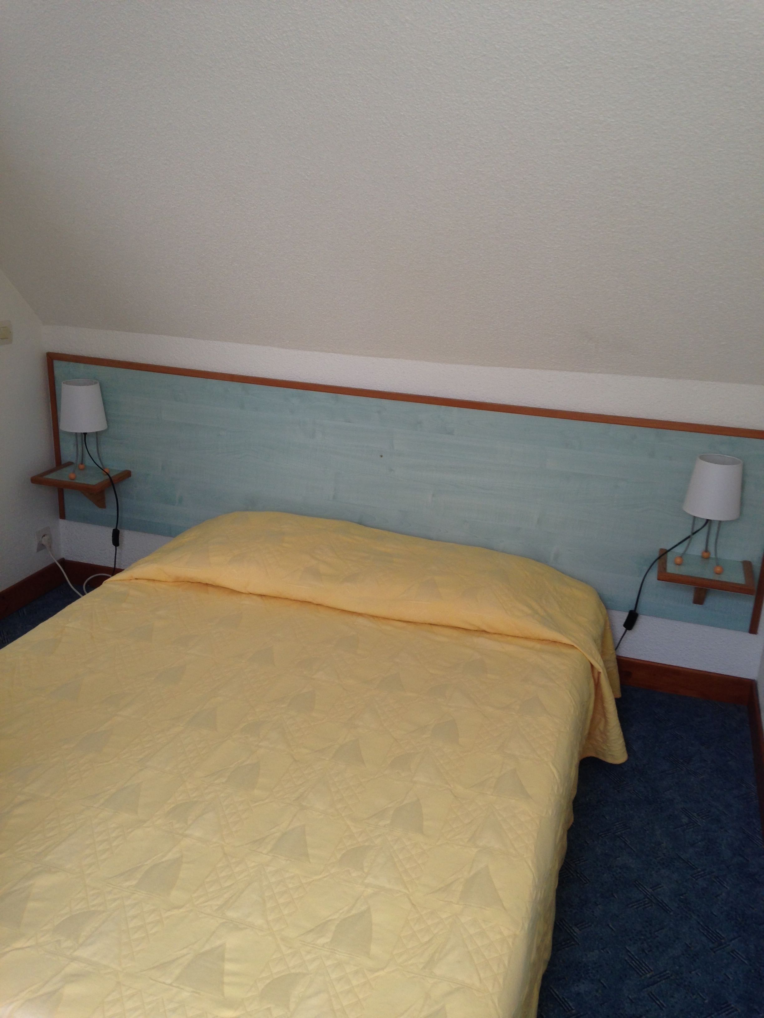 A bed with a patterned bedspread, a wooden headboard, and two bedside lamps on wooden nightstands.