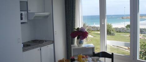 A dining area with a table set for breakfast, a view of the ocean, and a kitchen area.