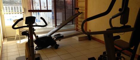 Un gimnasio con equipo de ejercicio, una ventana con persianas y vistas al balcón exterior.