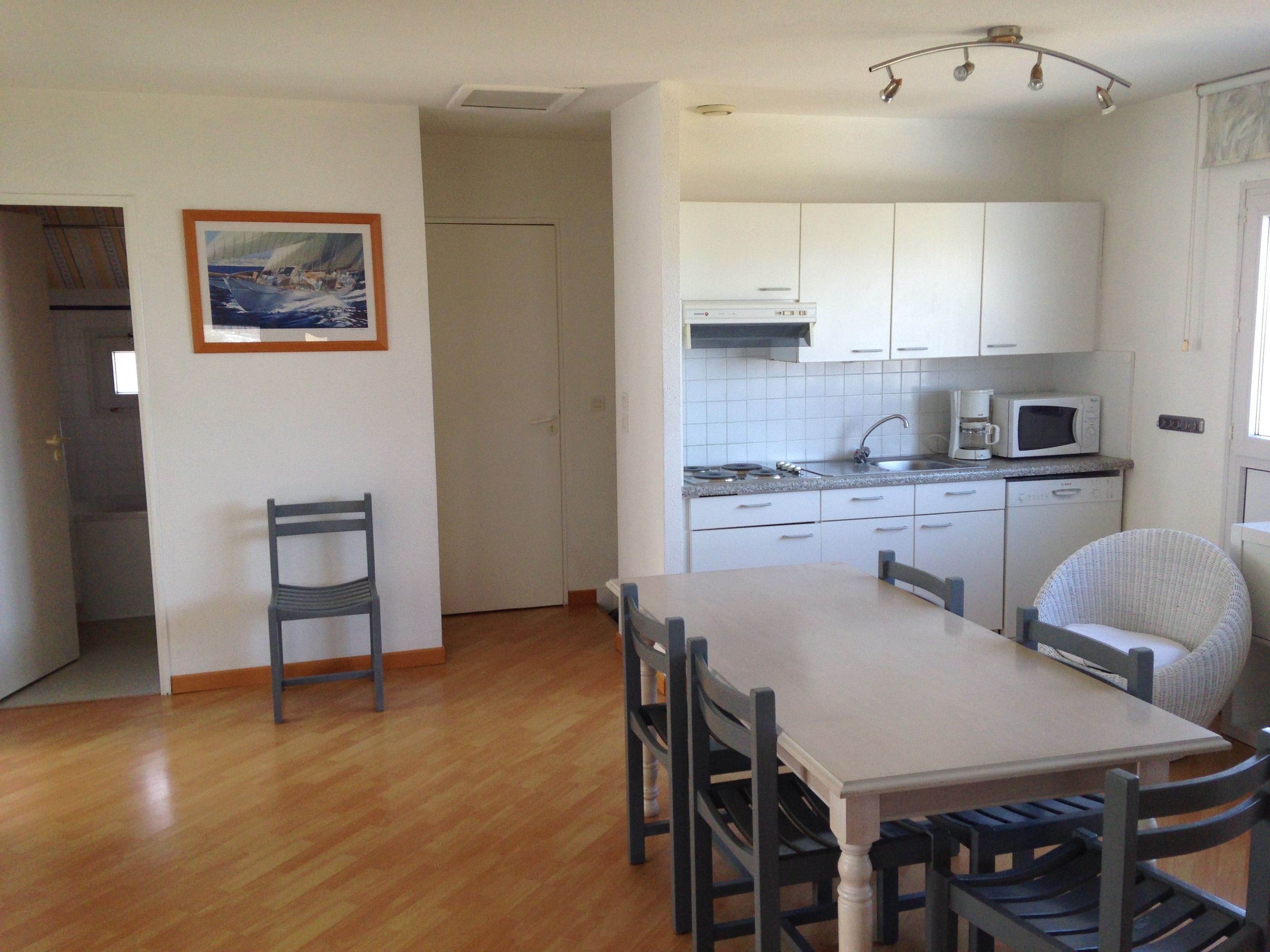 Una cocina compacta con armarios blancos, un microondas y un comedor con mesa y sillas.