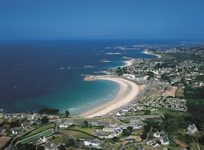 An aerial view of a coastal town with a curved beach, residential areas, and a clear view of the ocean.