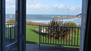Blick vom Balkon auf einen Strand mit Wellen, einer Rasenfläche und einem Metallzaun.