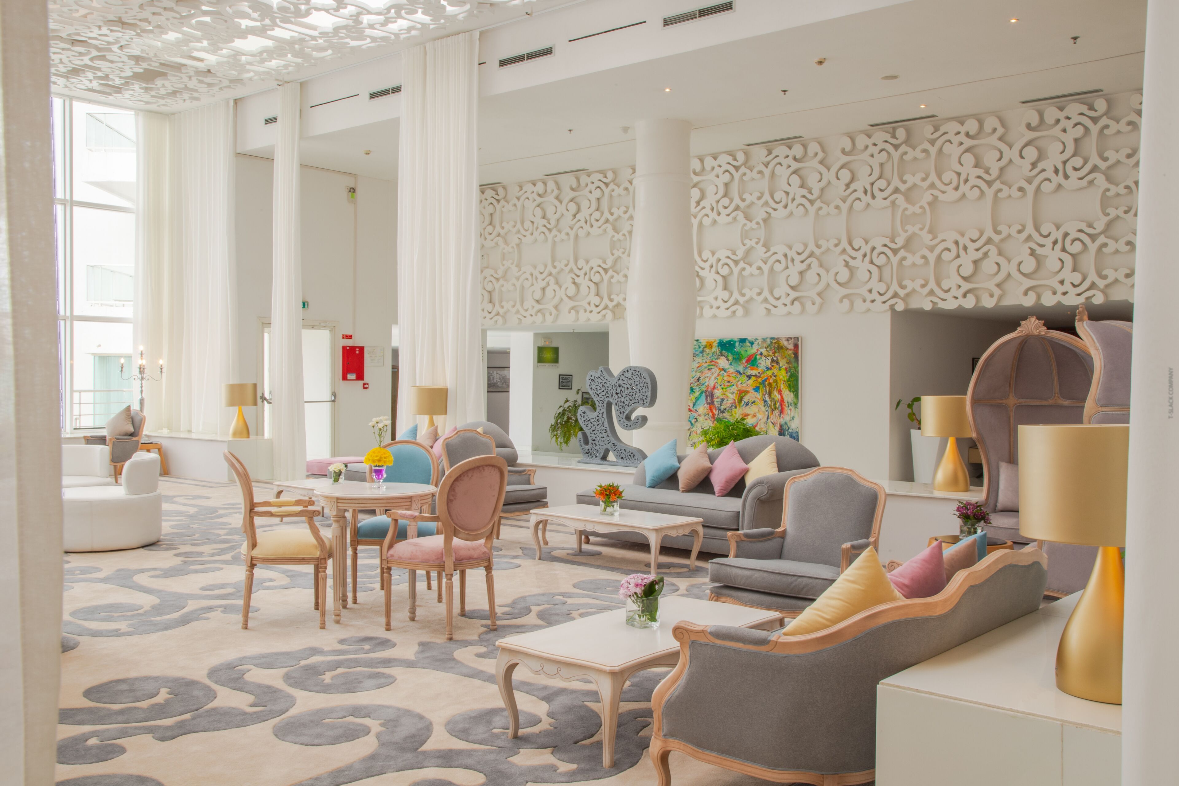 Un hall d’entrée spacieux au design moderne, comprenant un grand espace salon avec des canapés et des fauteuils, une table basse et un mur décoratif orné de motifs complexes.