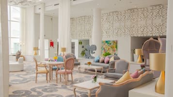 Un hall d’entrée spacieux au design moderne, comprenant un grand espace salon avec des canapés et des fauteuils, une table basse et un mur décoratif orné de motifs complexes.