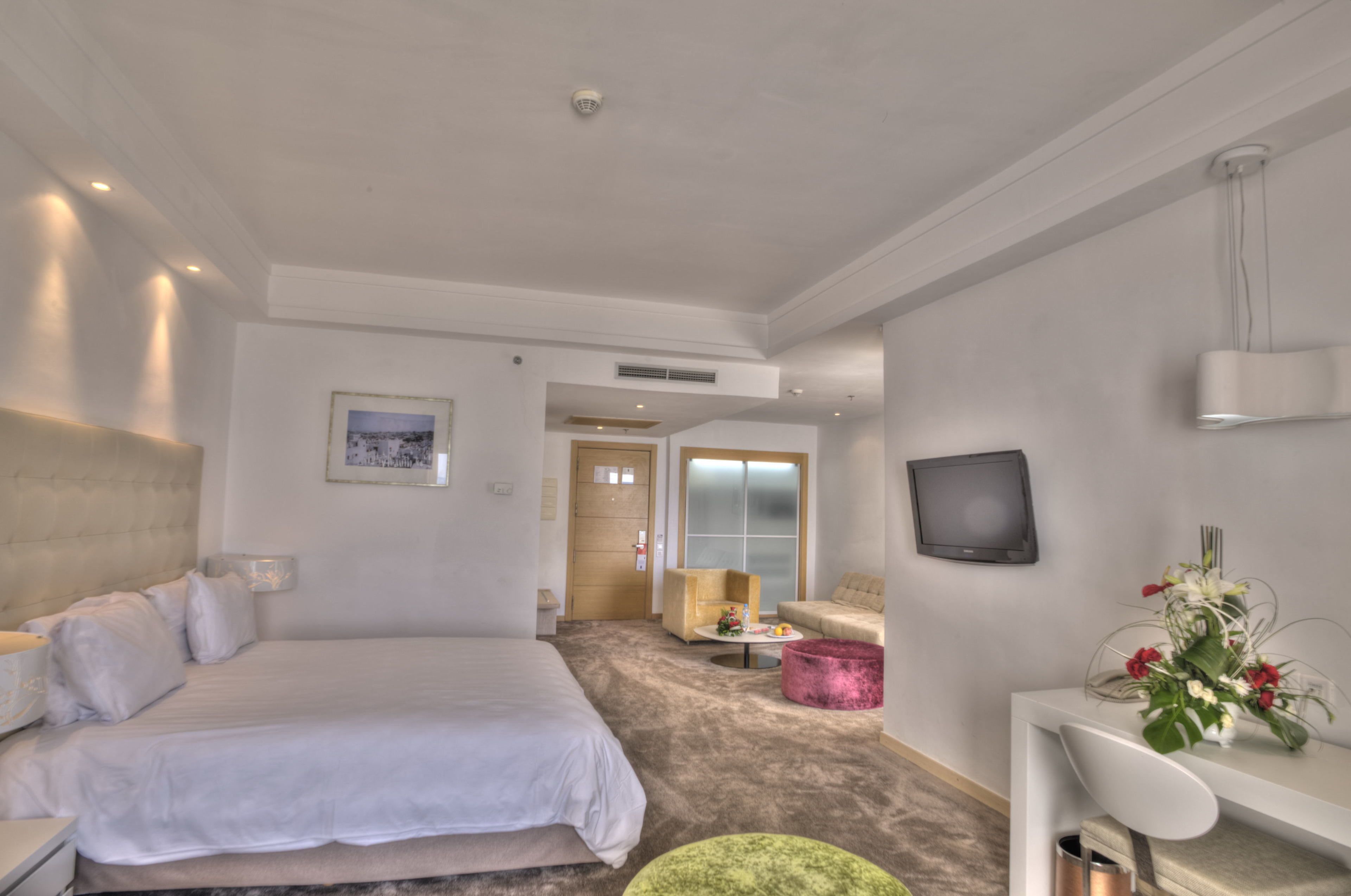 Una habitación de hotel con una cama grande, un escritorio, una silla, un televisor y una pequeña mesa con un jarrón de flores.