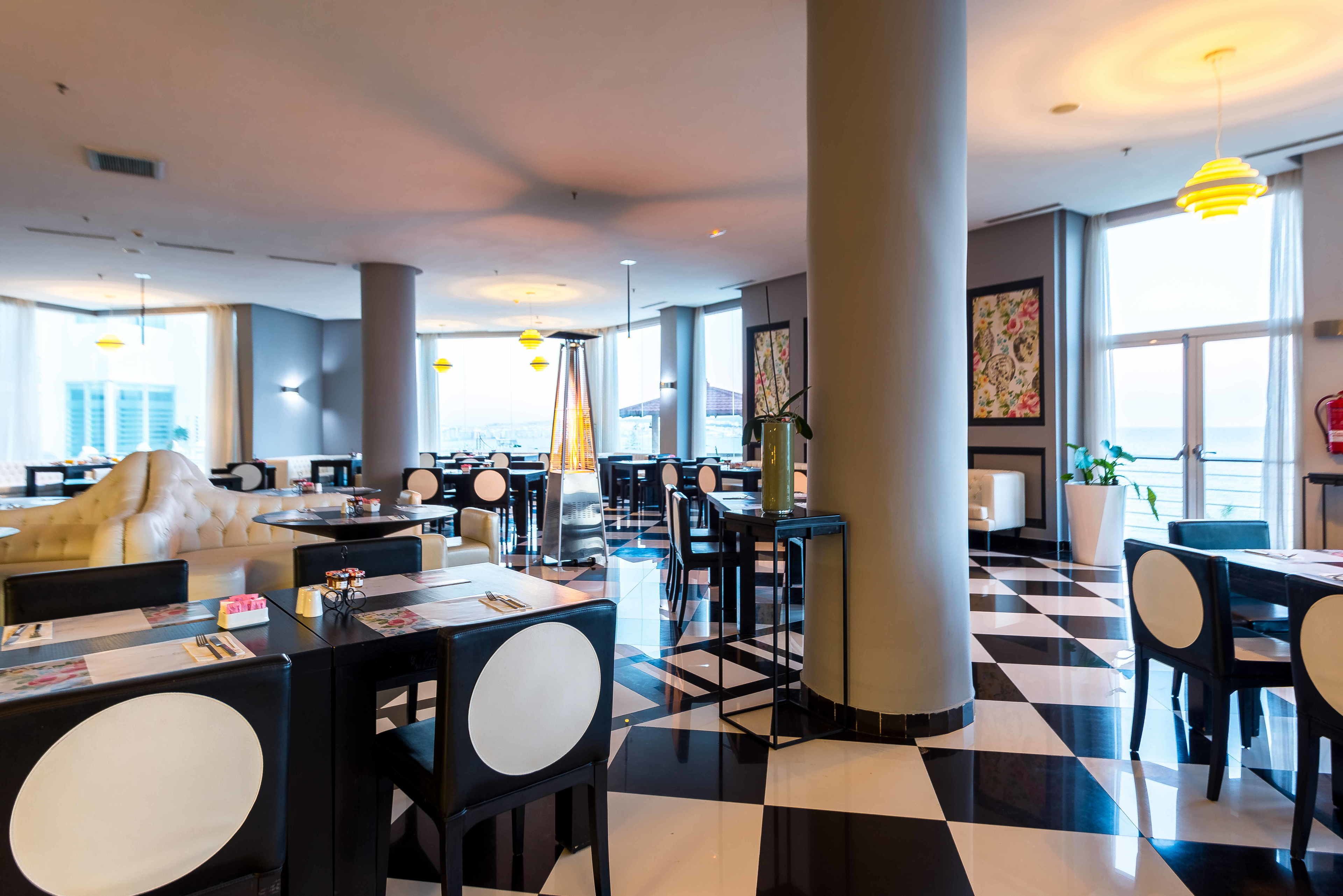A modern restaurant with black and white checkered flooring, round tables, and chairs.