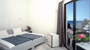 A modern bedroom with two beds, a small bedside table, a nightstand, and a large window with a view of the sea. - Akasti Hotel (Chania)