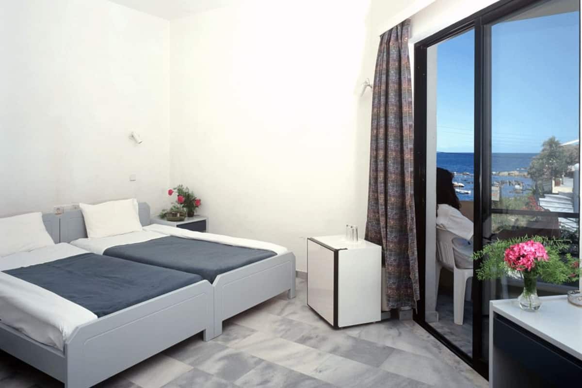 Un dormitorio moderno con dos camas, una mesita de noche pequeña, una mesita auxiliar y un ventanal con vista al mar.