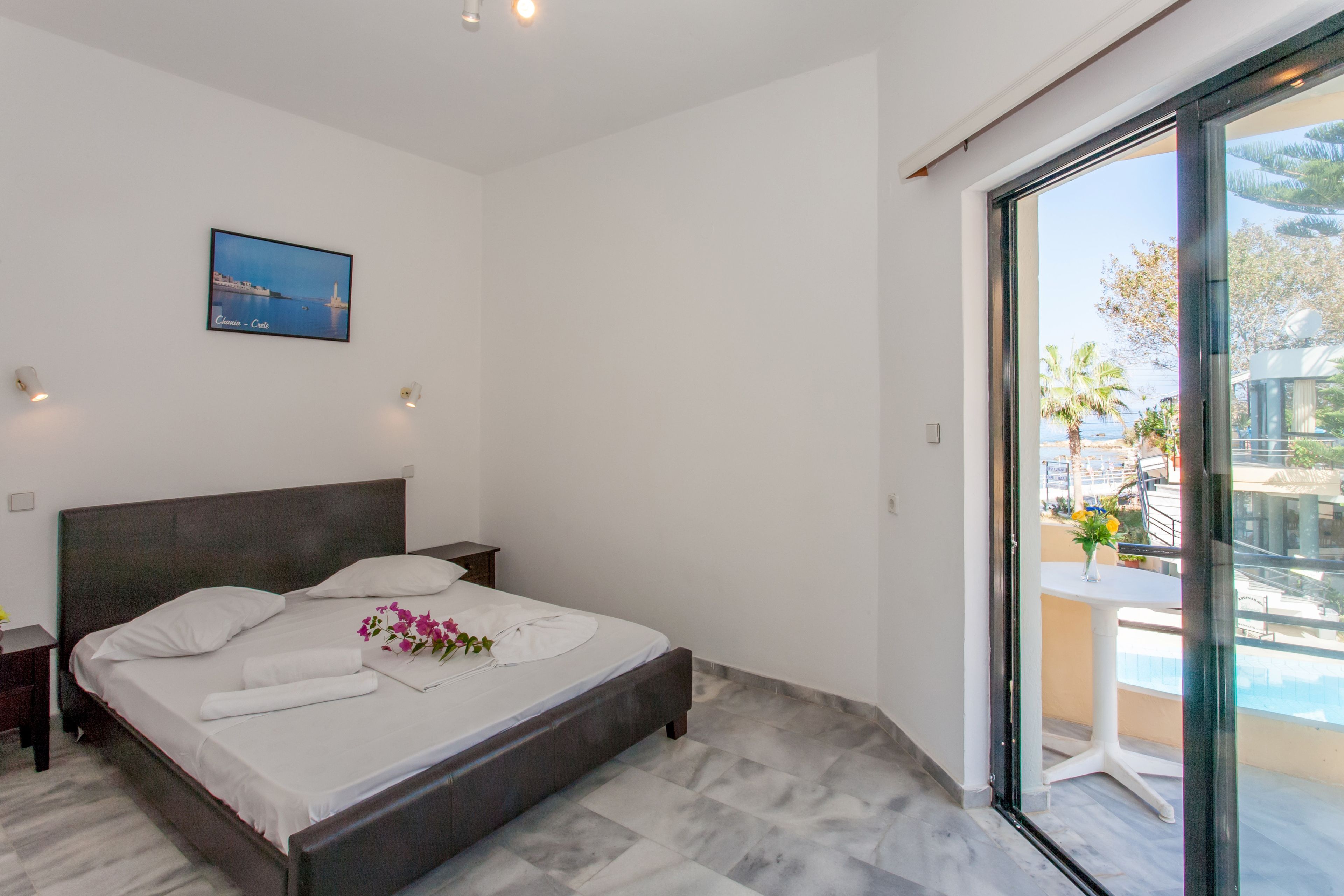 Ein modernes Schlafzimmer mit einem großen Bett, einem Nachttisch, einem Wandbild und einem Balkon mit Blick.