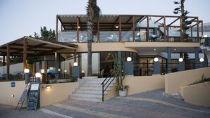 A modern building with a glass facade, outdoor seating, and a staircase leading to an upper level. - Akasti Hotel (Chania)