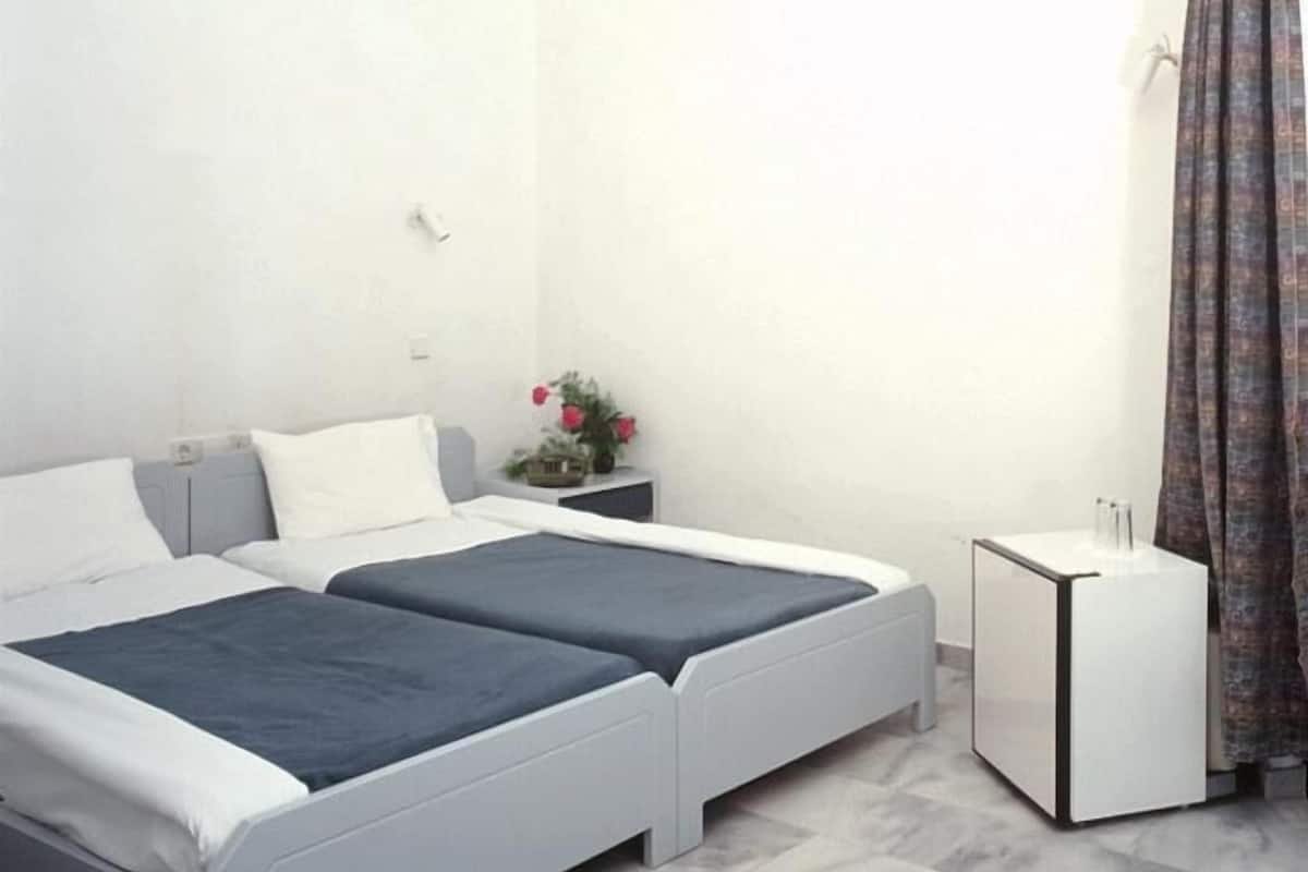 Un dormitorio con dos camas individuales, una mesita de noche con lámpara, un armario pequeño y una ventana con cortinas.