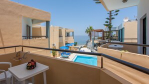 A balcony with a pool, white chairs, and blue umbrellas. - Akasti Hotel (Chania)