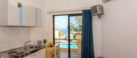 Cocina compacta con comedor, cama pequeña y balcón con vista a la piscina.