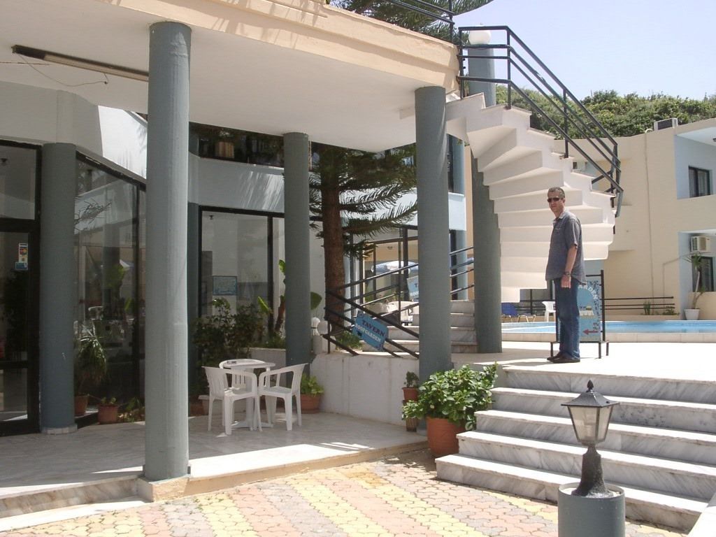 A hotel entrance with a staircase, outdoor seating, and a pool in the background.