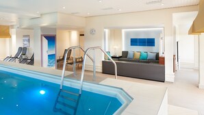 A modern indoor swimming pool with a clear view of the lounge area, a sofa, and a wall-mounted clock. - Best Western Plus Arosa Hotel (Paderborn)