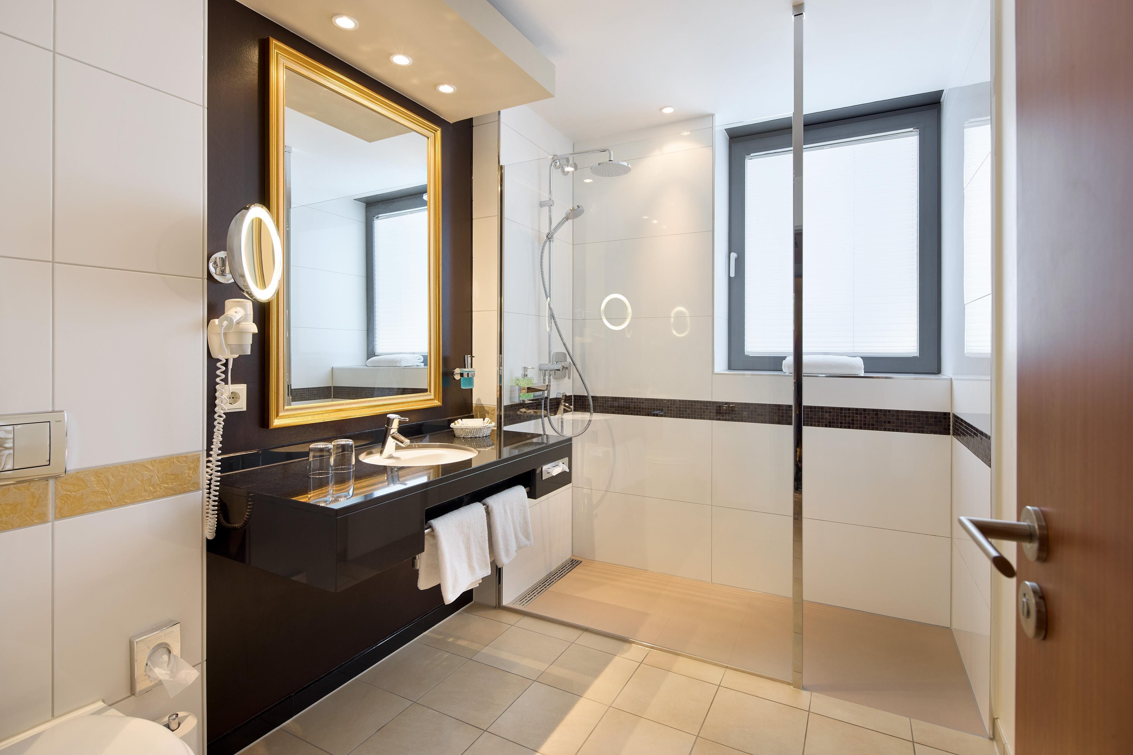 Ein modernes Badezimmer mit großem Spiegel, Waschtisch und Dusche mit Glastüren. Ein Fenster sorgt für natürliches Licht.