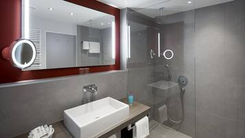 A modern bathroom with a large mirror, a white sink, a glass shower enclosure, and a red accent wall.