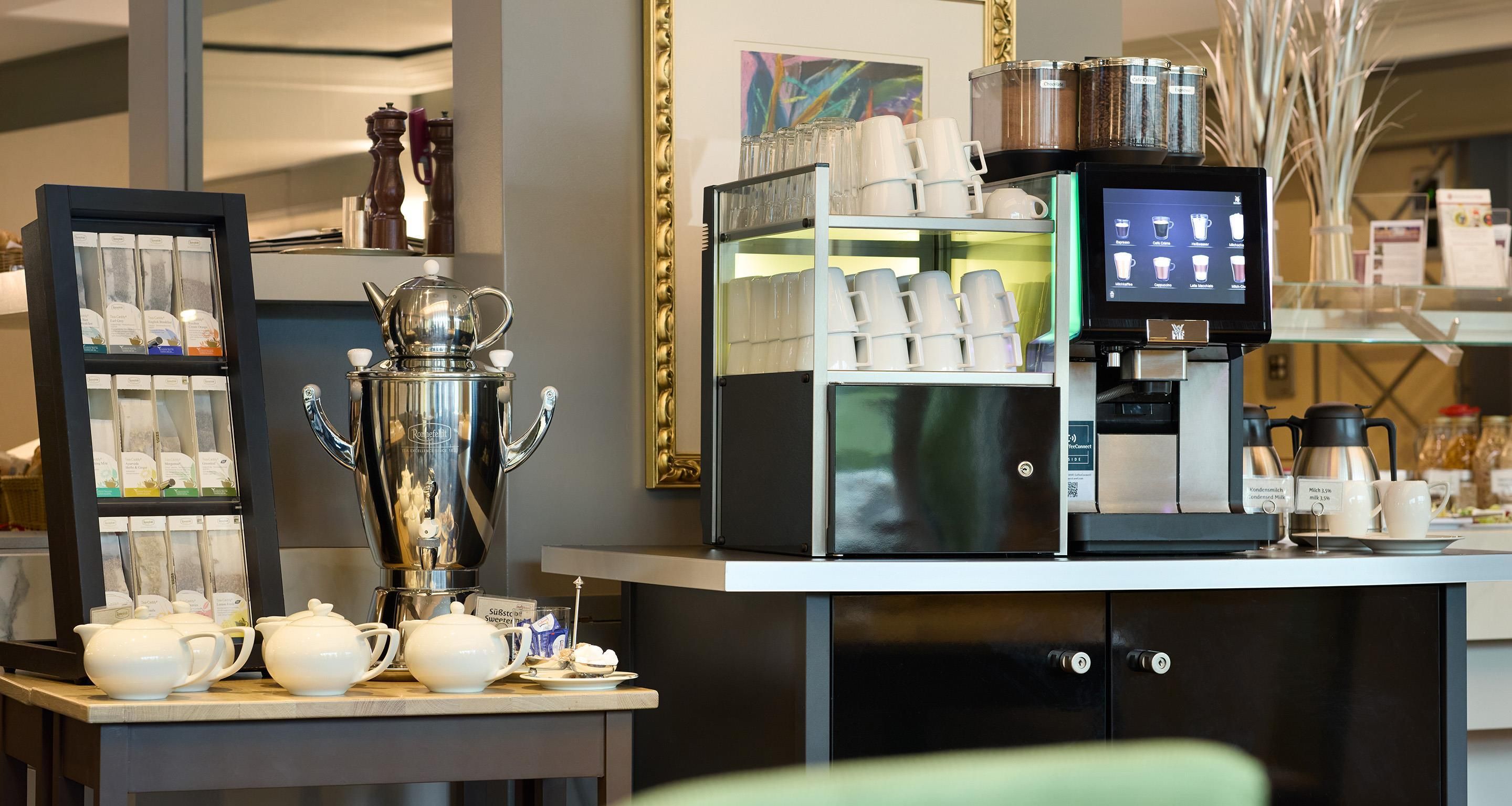 Kaffestation med kaffemaskine, udvalg af kaffekapsler og et udstilling af kaffekopper.