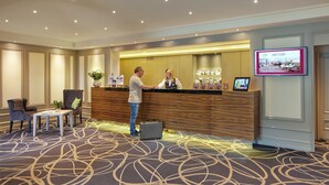 A hotel reception area with a wooden reception desk, a digital screen displaying the first floor, and a carpeted floor with a geometric pattern. - Best Western Plus Arosa Hotel (Paderborn)