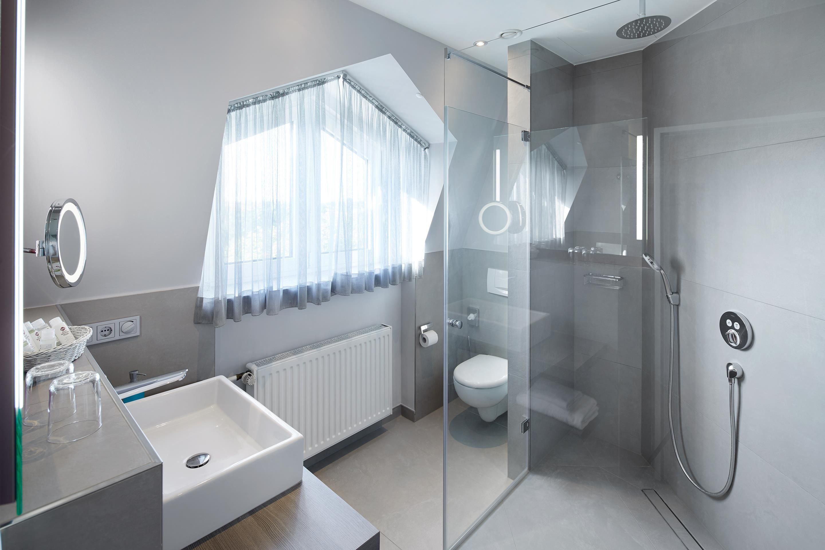 Een moderne badkamer met een douchecabine van glas, een witte wastafel en een toilet.
