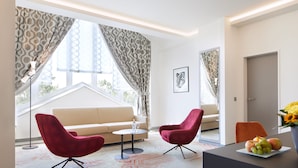 A modern living room with a sofa, two red chairs, a small table, and a fruit bowl. - Best Western Plus Arosa Hotel (Paderborn)