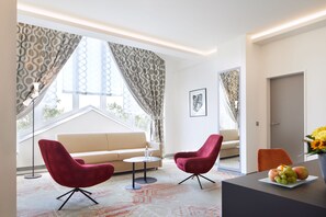 A modern living room with a sofa, two red chairs, a small table, and a fruit bowl. - Best Western Plus Arosa Hotel (Paderborn)