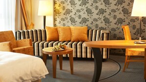 A hotel room with a striped sofa, two armchairs, a round wooden table, and a bed with a white duvet. - Best Western Plus Arosa Hotel (Paderborn)