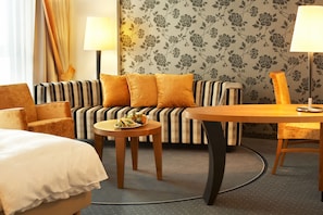 A hotel room with a striped sofa, two armchairs, a round wooden table, and a bed with a white duvet. - Best Western Plus Arosa Hotel (Paderborn)