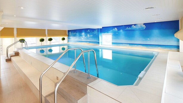 An indoor swimming pool with a view of the sea, a staircase leading to the pool, and a ceiling with recessed lighting. - Best Western Plus Arosa Hotel (Paderborn)
