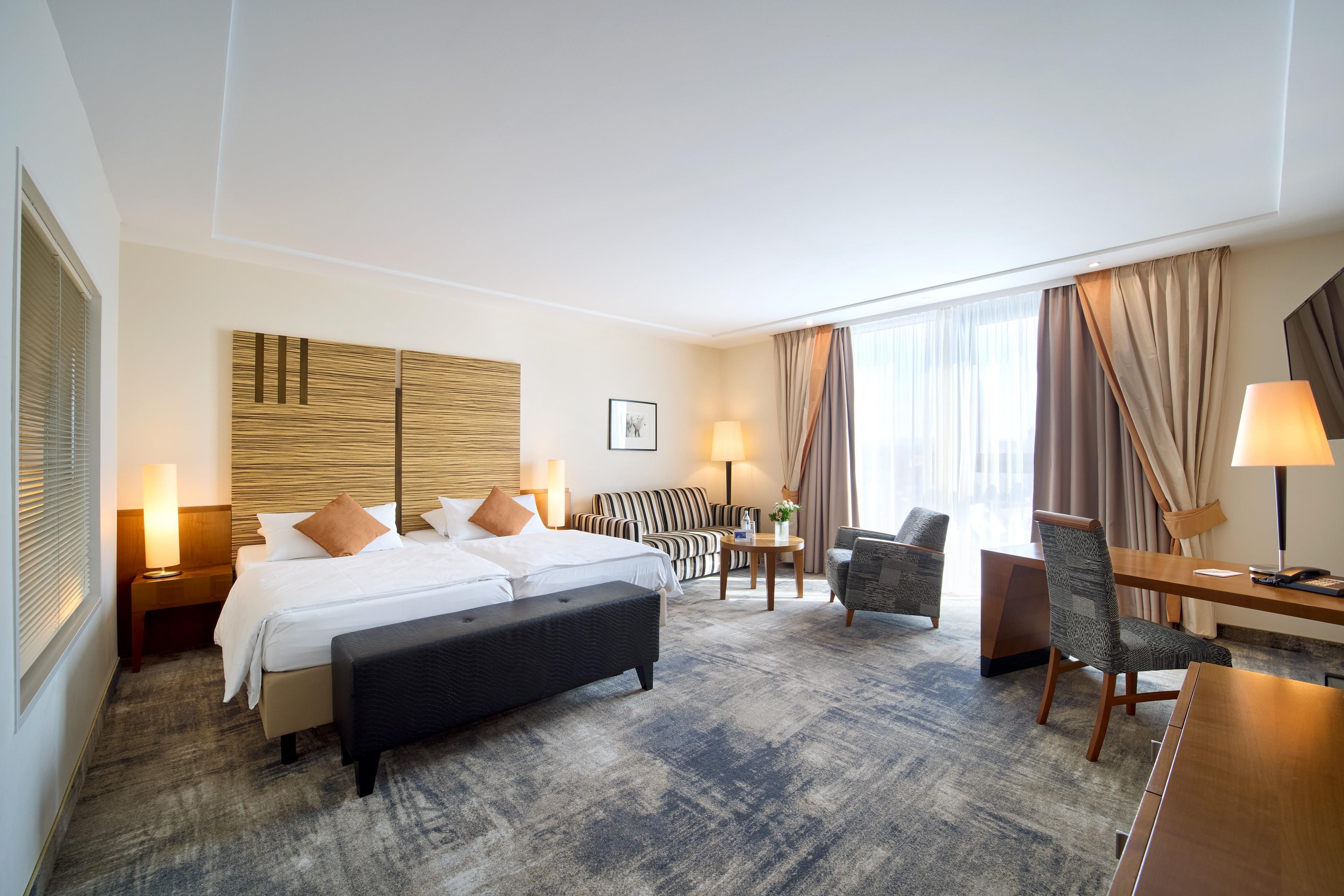 A hotel room with a bed, a sofa, a chair, a desk, and a lamp.
