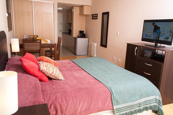 Une chambre avec un lit, une télévision, un bureau et un coin cuisine.