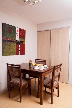 A dining area with a wooden table, four chairs, and a painting on the wall.