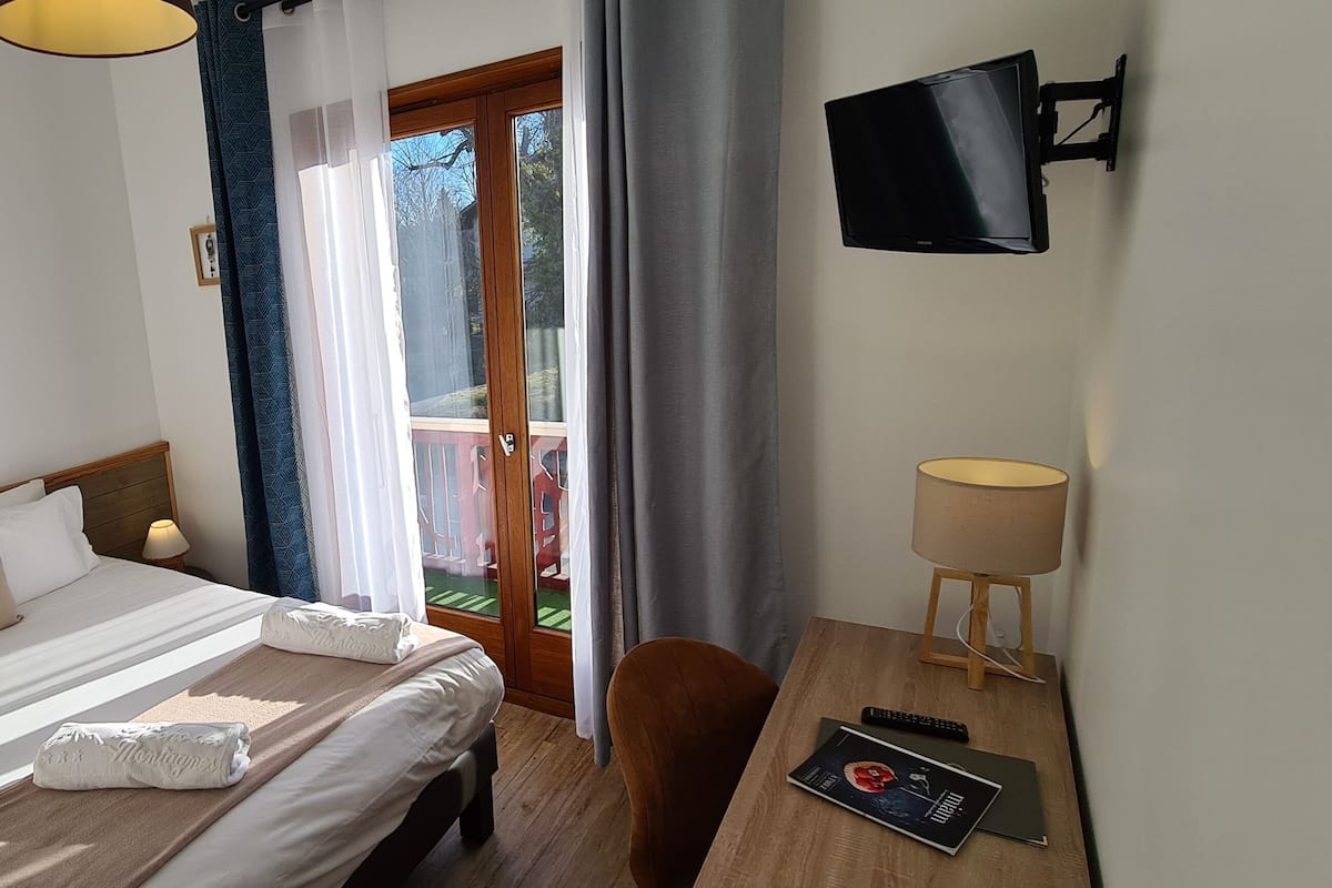 Une chambre d’hôtel avec un lit, un bureau avec une lampe, une télévision et une vue sur l’extérieur.